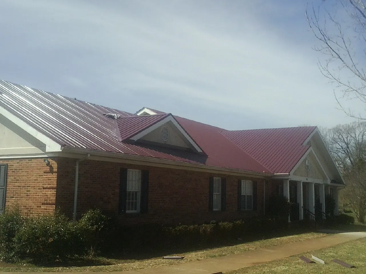 Red metal roof with gabled entries on a long brick building, from a Hail Damage Roof Repair job in Pauma Valley