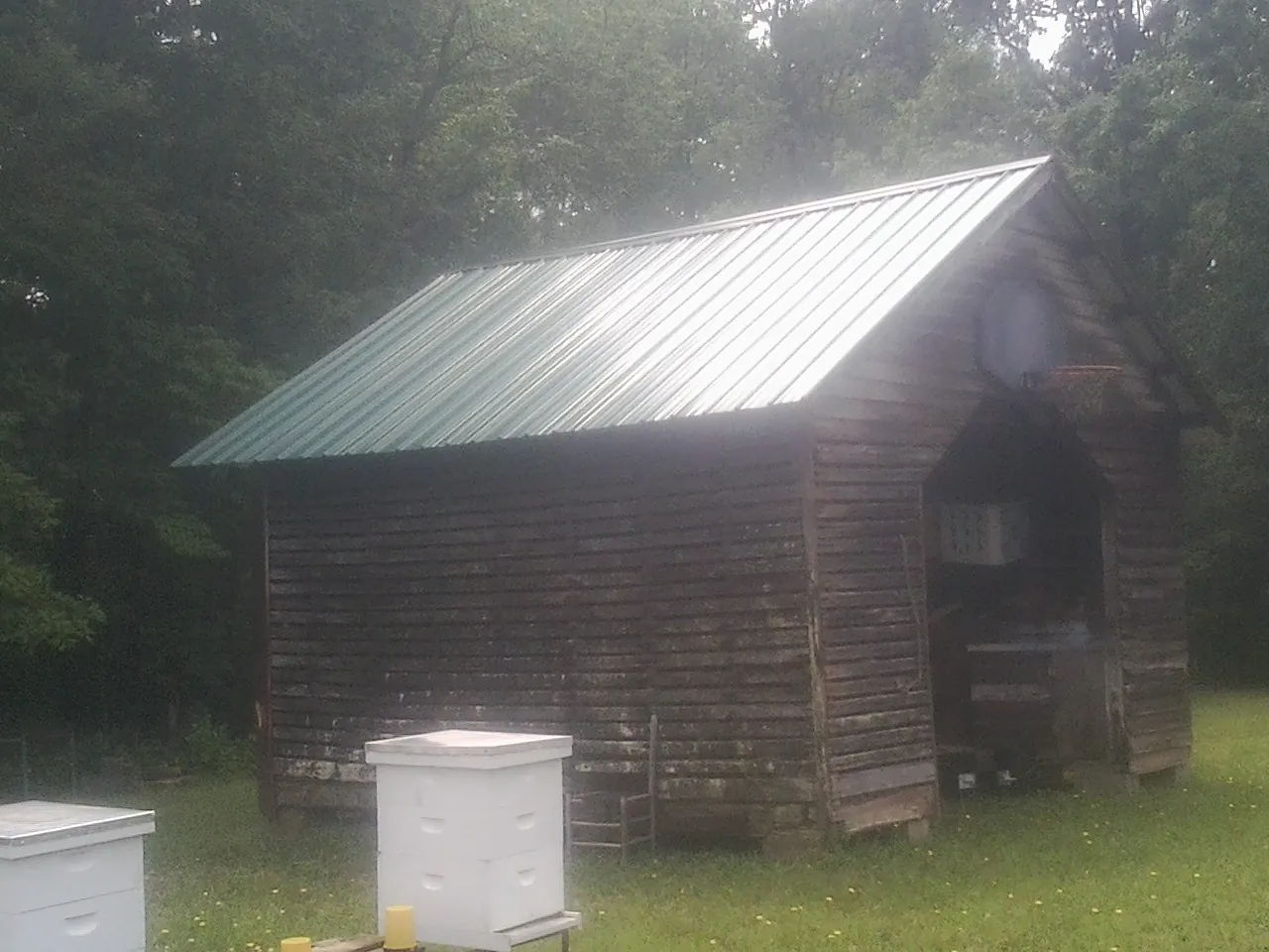 Green metal roof on a weathered barn beside stacked beehives in Pauma Valley