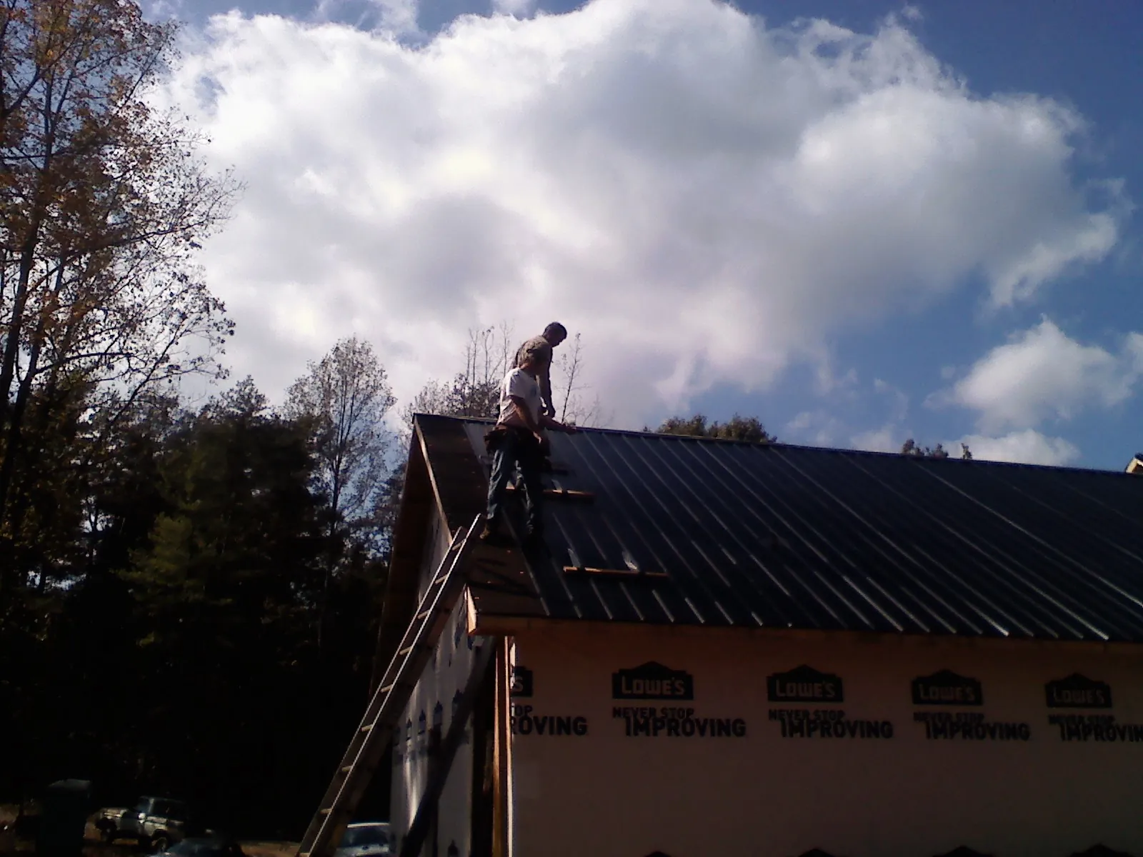Roofer fastening dark metal panels high against a cloudy sky, from a Roof Inspection job in Pauma Valley