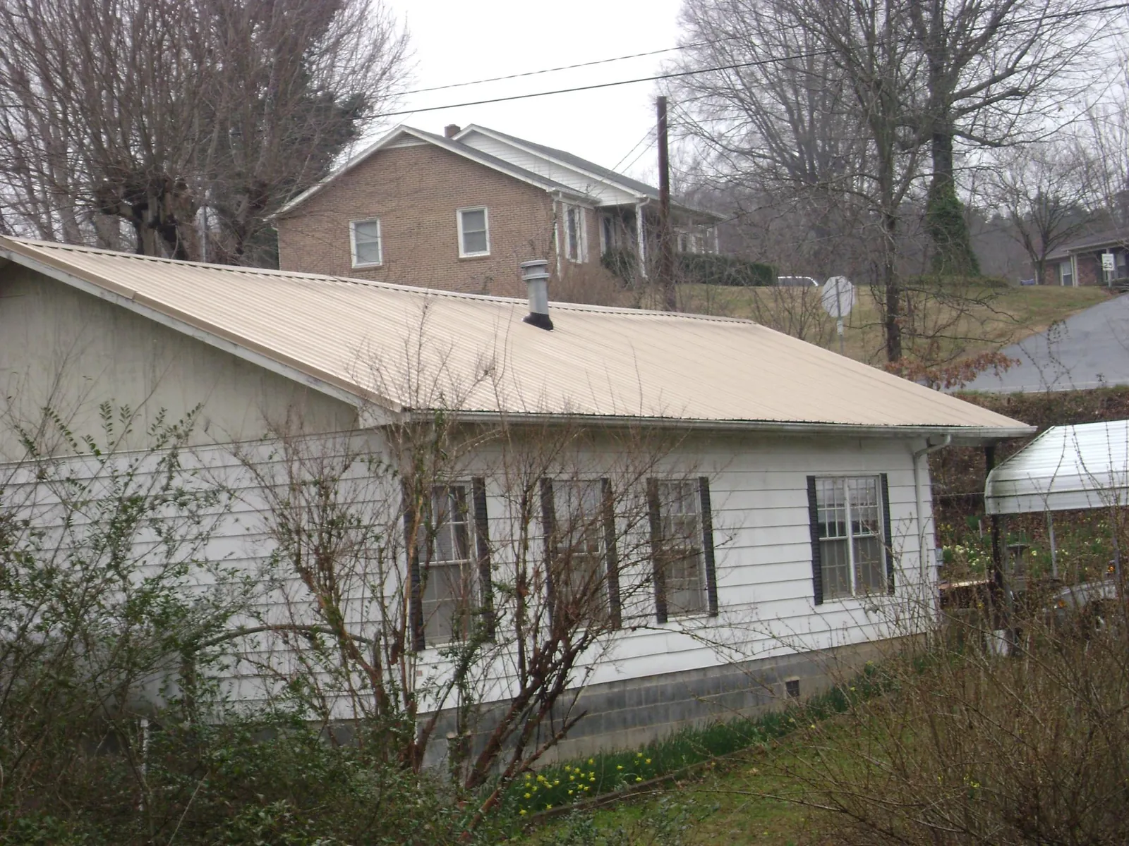 Tan metal roof on a white sided house set into a hillside — Commercial Roofing by Roofing Brothers in Pauma Valley